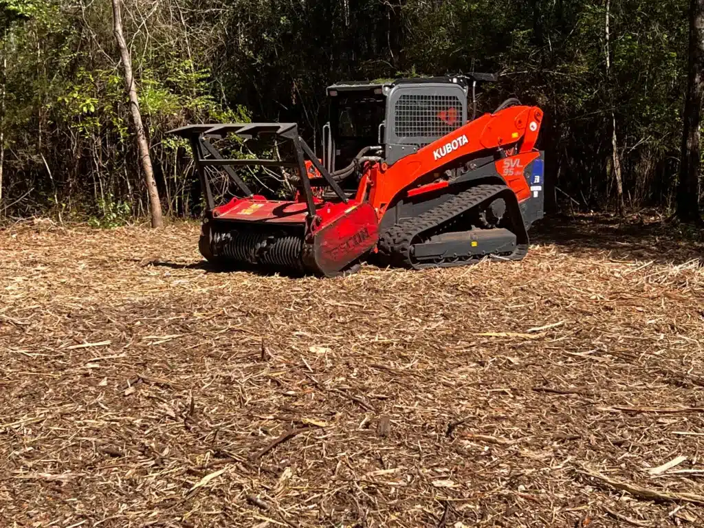 Red skid steer forestry mulcher clearing brush and overgrowth in a wooded area